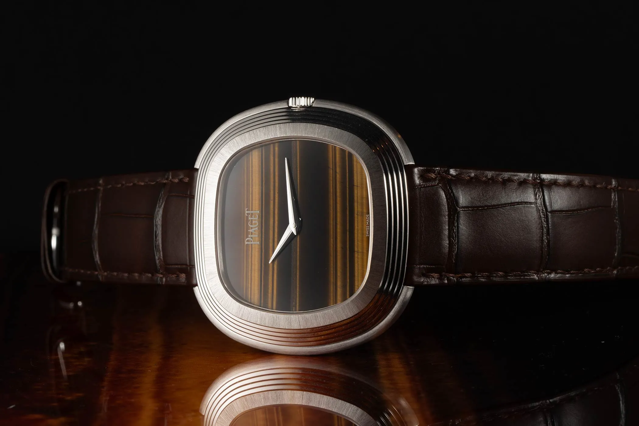 Piaget Andy Warhol watch with tiger's eye dial lying on the side on a wooden surface.