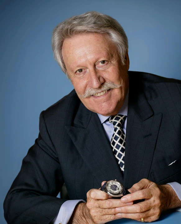 Portrait of Gérald Genta smiling while holding a Gerald Charles watch, symbolizing his legacy in Swiss luxury watchmaking.