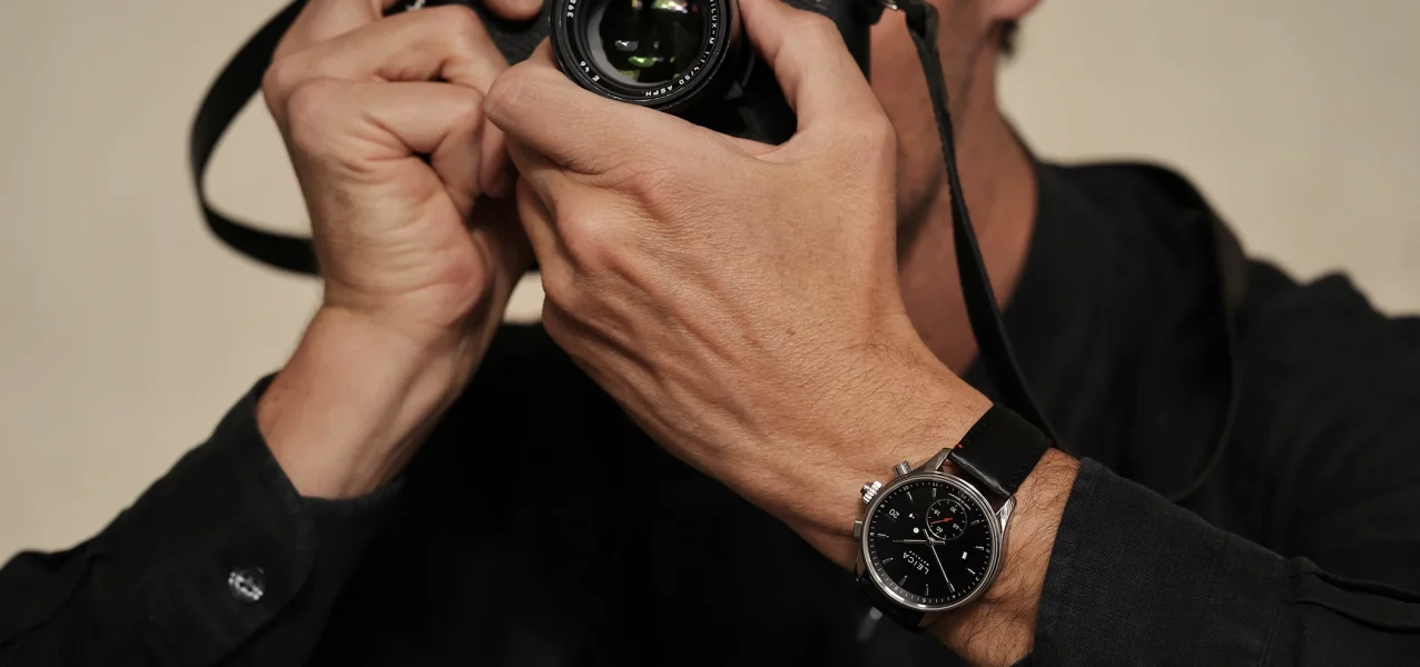 The Leica Camera ZM 2 watch with manual winding on the wrist alongside a camera, third view.