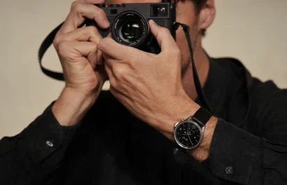 The Leica Camera ZM 2 watch with manual winding on the wrist alongside a camera, third view.