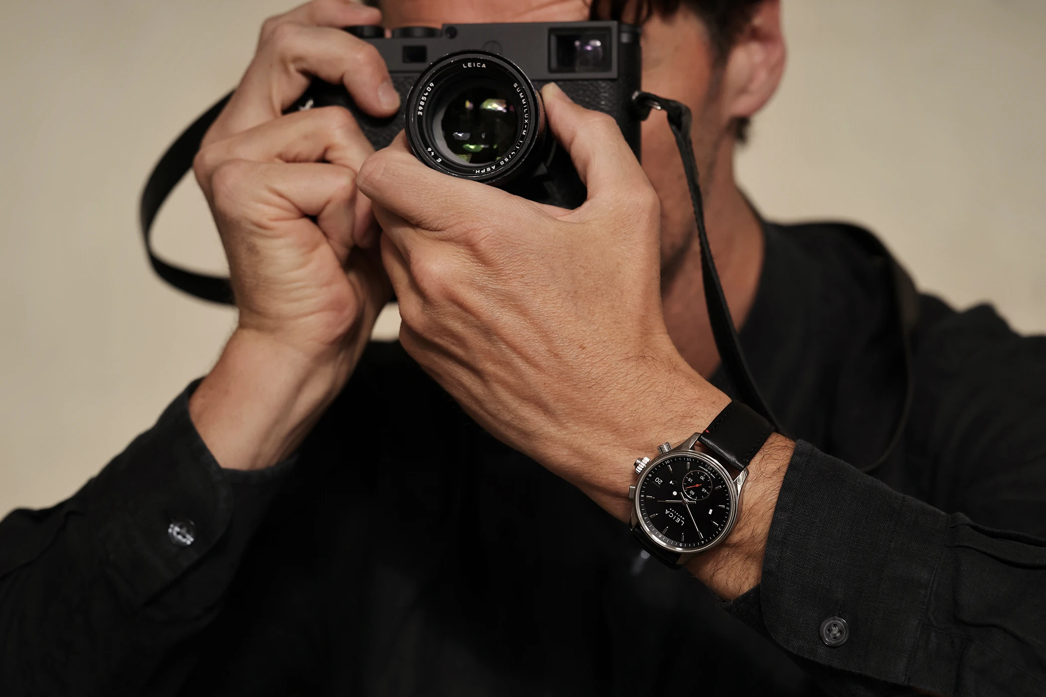 The Leica Camera ZM 2 watch with manual winding on the wrist alongside a camera, third view.