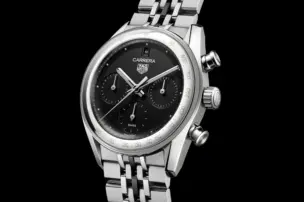 The TAG Heuer Carrera Chronograph with a black dial, three subdials and a stainless steel case on a multi-link steel bracelet against a black background, shown from the front.