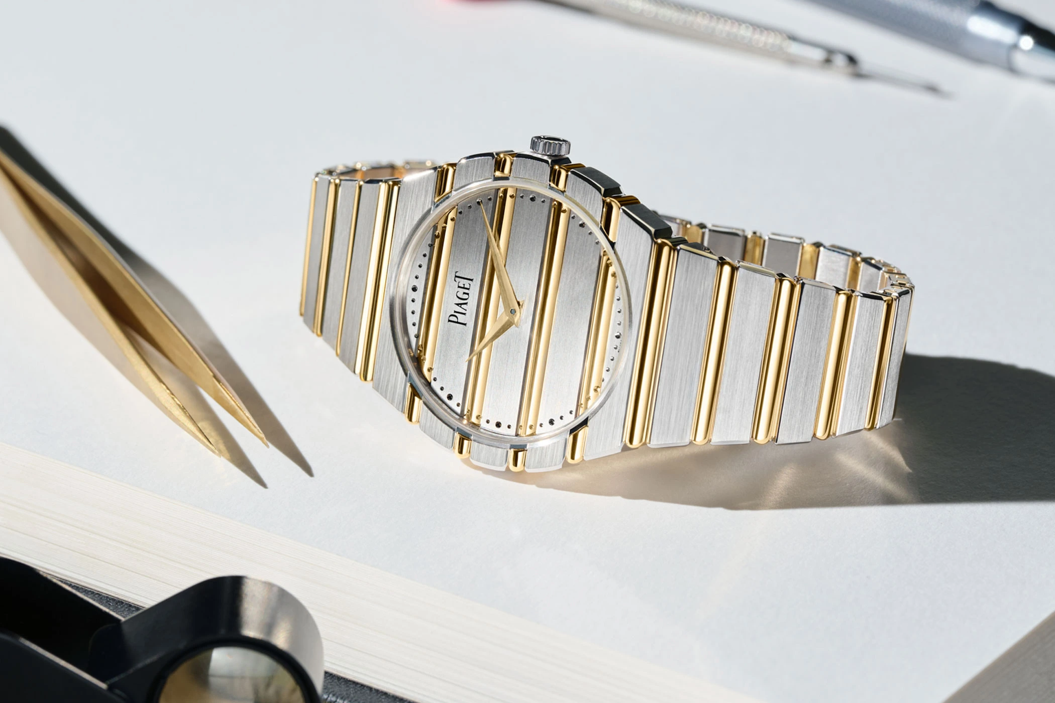 Piaget Polo 79 Two Tone lying on its side next to tweezers and a magnifying glass