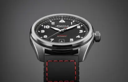 Close-up of the dial of the Alpina Startimer Pilot Automatic with black dial and black Cordura strap against a grey background.