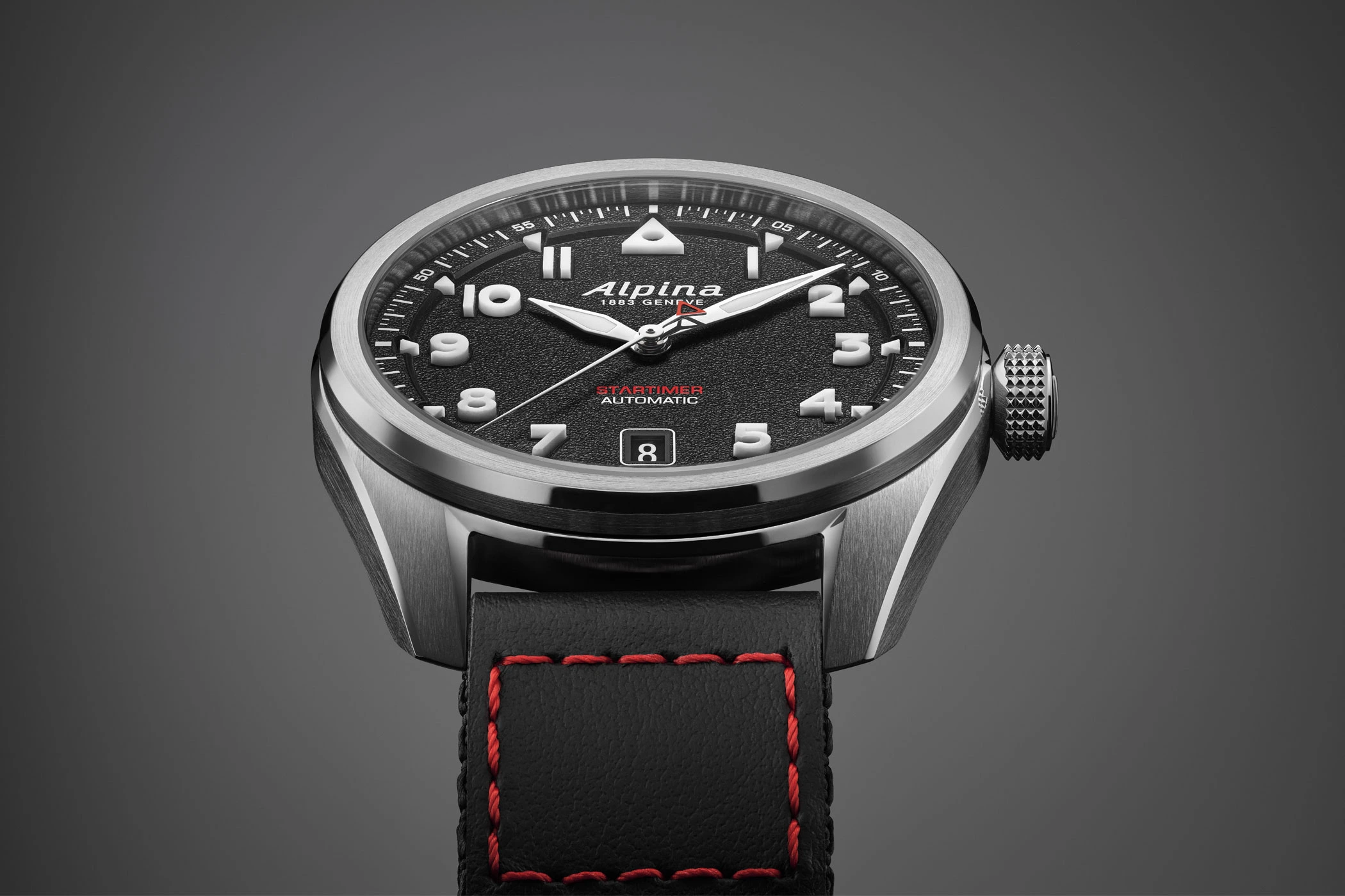 Close-up of the dial of the Alpina Startimer Pilot Automatic with black dial and black Cordura strap against a grey background.