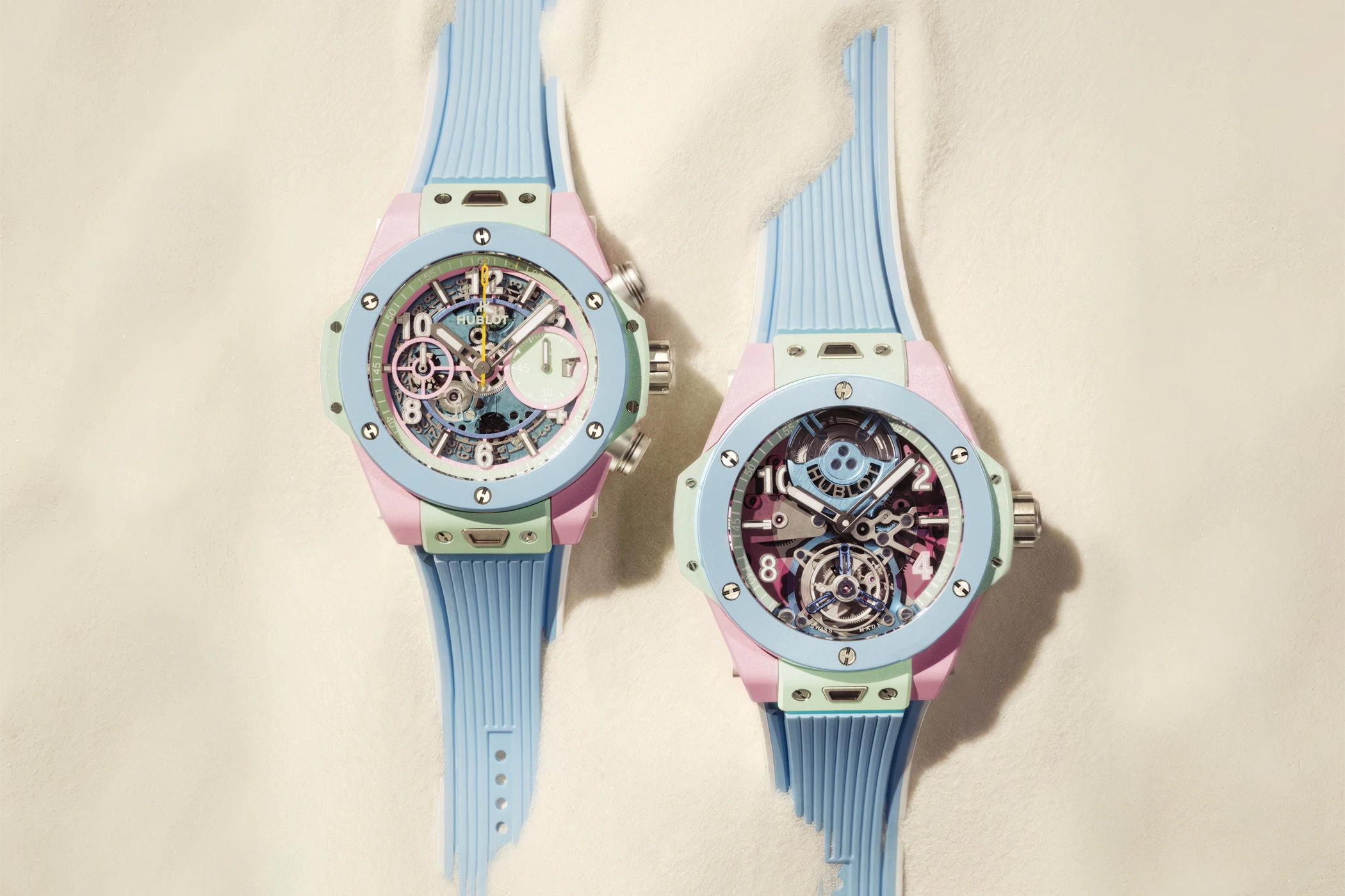 The Big Bang Summer Multi-Colored Ceramic 42 mm and Big Bang Summer Multi-Colored Ceramic 44 mm are lying in the sand; the straps are partially covered.