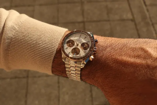 An Omega Speedmaster 38 mm from the 2026 model year, in a two-tone design featuring Sedna gold and a brown bezel, can be seen on the wrist.