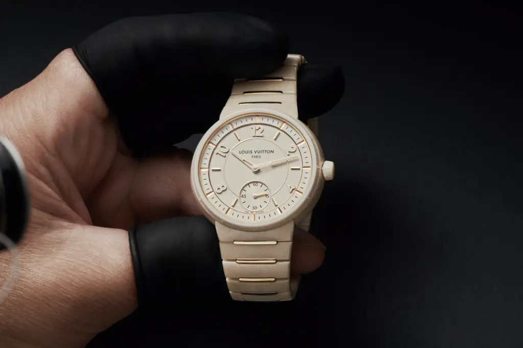A Louis Vuitton Tambour watch in white ceramic and yellow gold can be seen in the hands of a watchmaker.